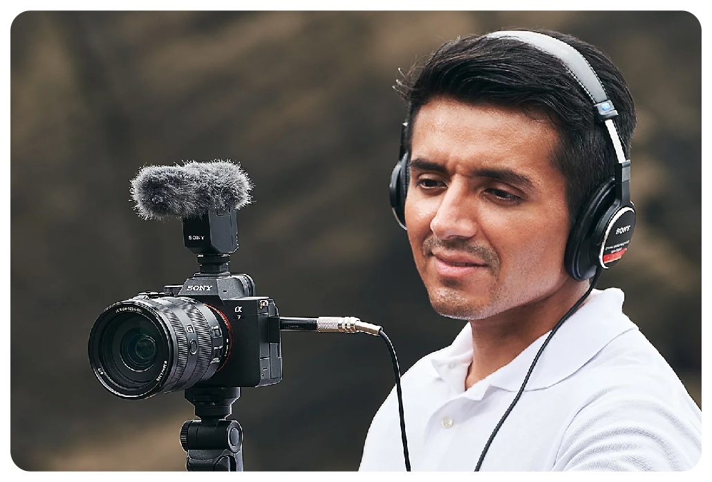 Filmaker wearing monitor headphones connected to Sony A7IV camera with external microphone